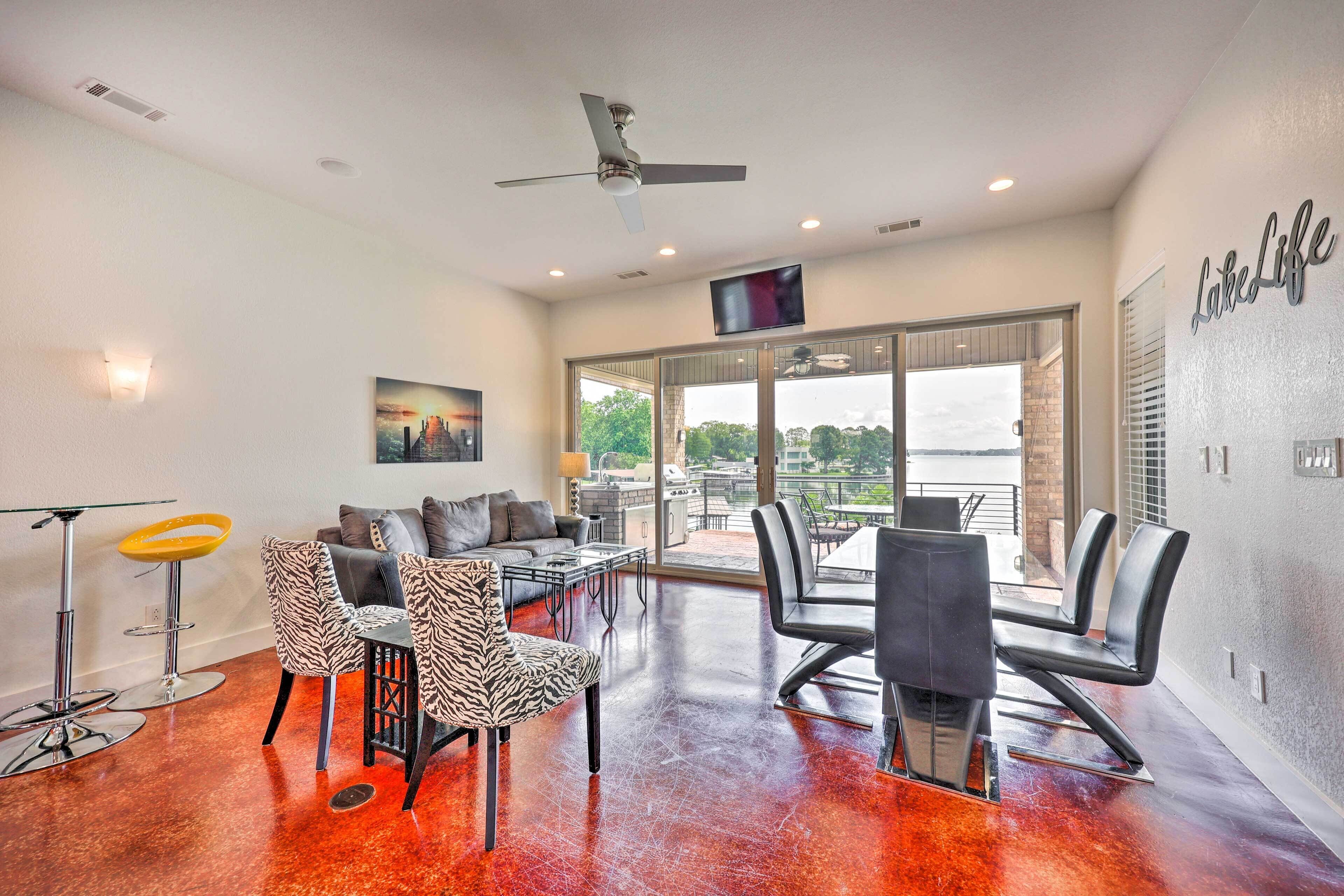 A modern living room with a glass door leading to a balcony, a ceiling fan, and a flat-screen TV mounted on the wall.