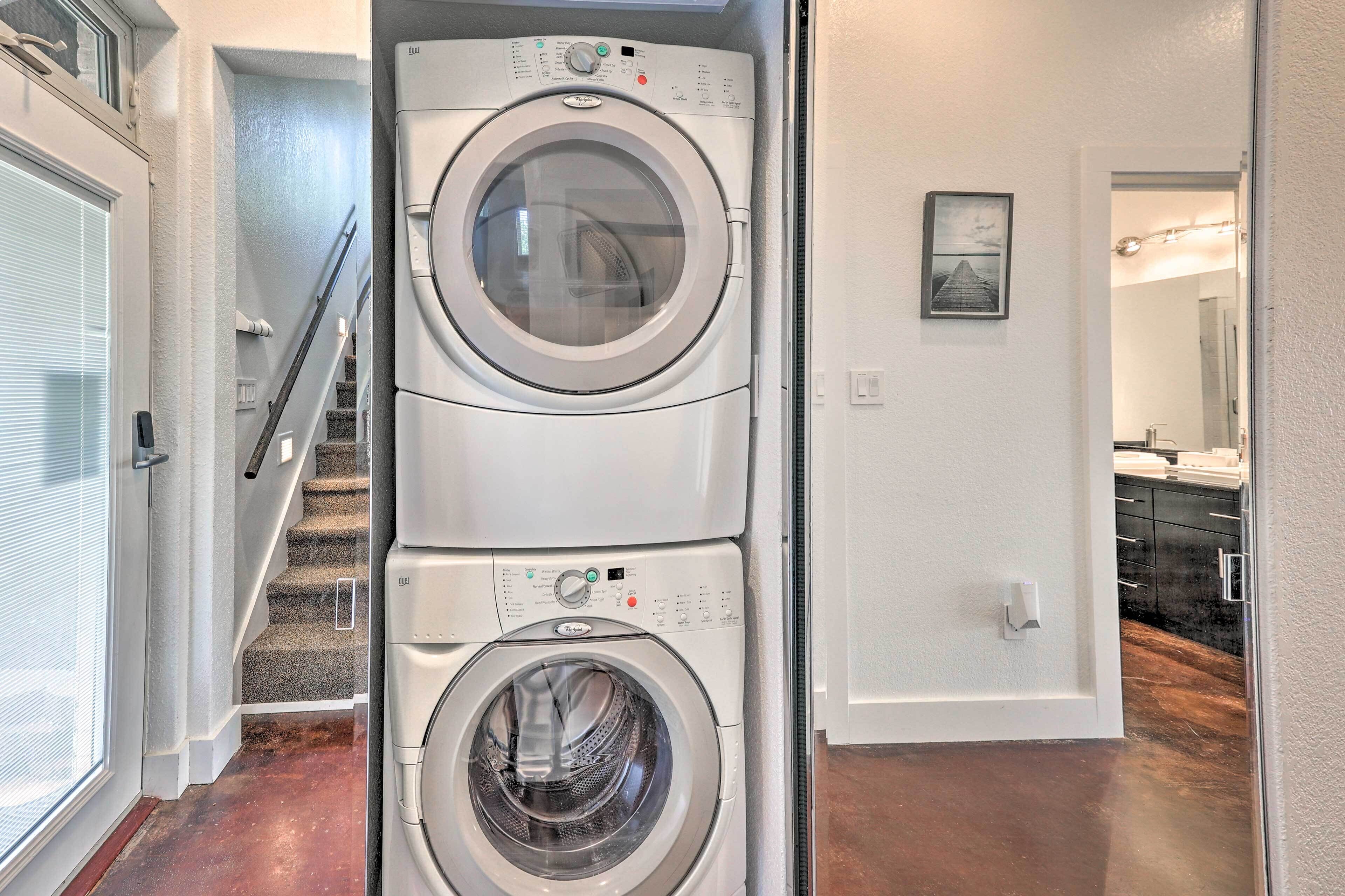 A laundry room with two stacked front-loading washing machines and a staircase leading to another room.