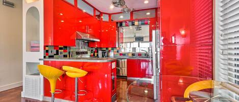 A modern kitchen with red cabinetry, stainless steel appliances, and a glass island with yellow bar stools.