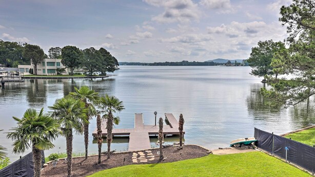 A lakeside property with a dock, palm trees, and a grassy area. - Waterfront Home ~ 4 Mi to Oaklawn Racing Casino! (Hot Springs)