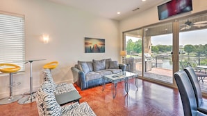 A modern living room with a grey sofa, a zebra-patterned couch, a glass coffee table, and a TV mounted on the wall. - Waterfront Home ~ 4 Mi to Oaklawn Racing Casino! (Hot Springs)