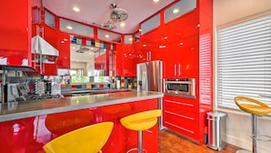 A modern kitchen with red cabinetry, stainless steel appliances, and a central island with yellow bar stools. - Waterfront Home ~ 4 Mi to Oaklawn Racing Casino! (Hot Springs)