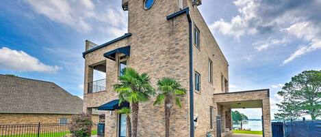 A modern two-story building with a brick facade, a covered patio area, and a view of a body of water.