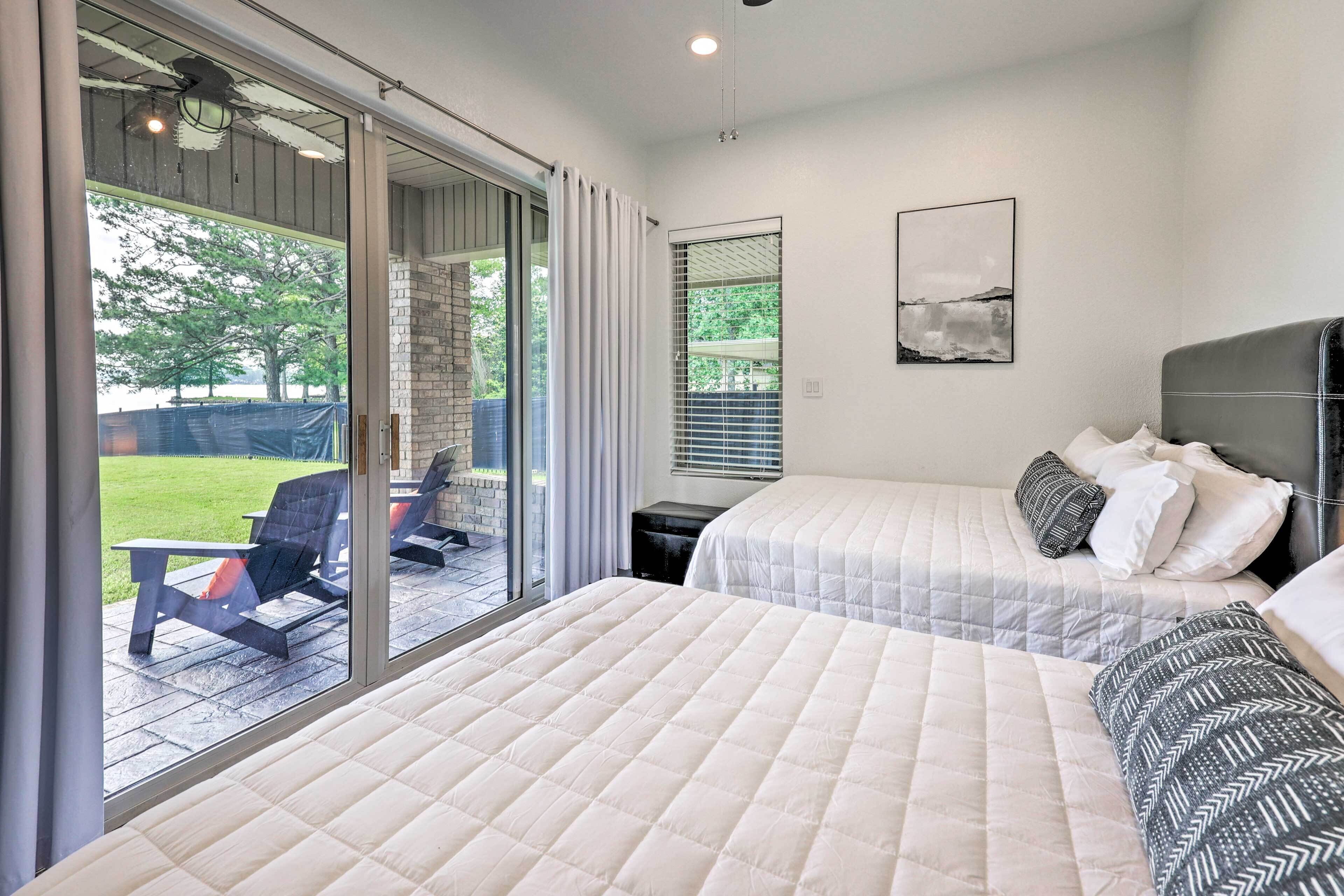 A modern bedroom with two beds, a large sliding glass door leading to an outdoor area, and a framed picture on the wall.