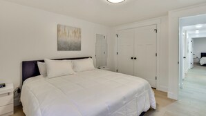 A bedroom with a large bed, a bedside table, a nightstand, a ceiling light, a wardrobe, and a mirror. - Sleek & Modern Morgan Abode: Great for Families! (Morgan)