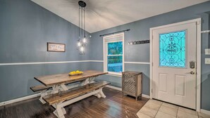 A dining area with a wooden table and benches, a hanging light fixture, a door with a decorative glass panel, and a window with a view of greenery. - Peaceful Sevierville Home w/ Private Hot Tub! (Sevierville)