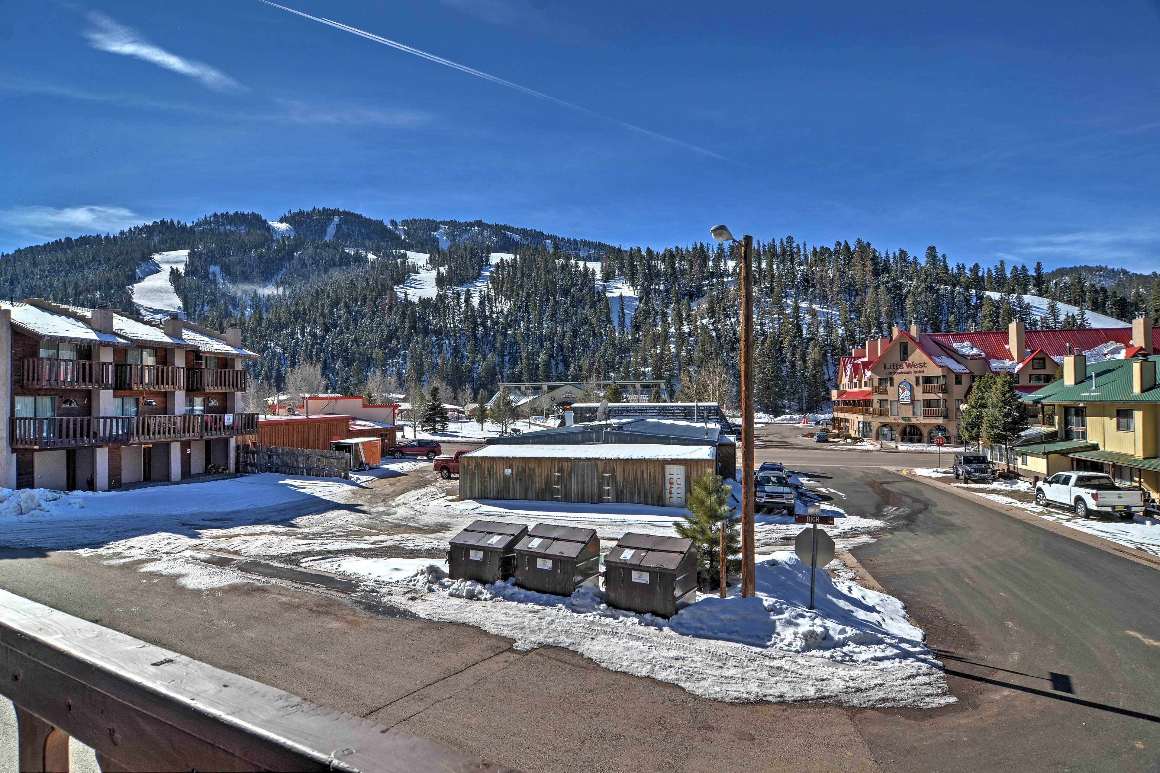 A hotel with a snow-covered parking lot, a mountain backdrop, and a clear sky.