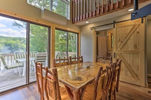 Un espace repas comprenant une grande table et des chaises en bois, de grandes fenêtres et une vue sur une terrasse.
