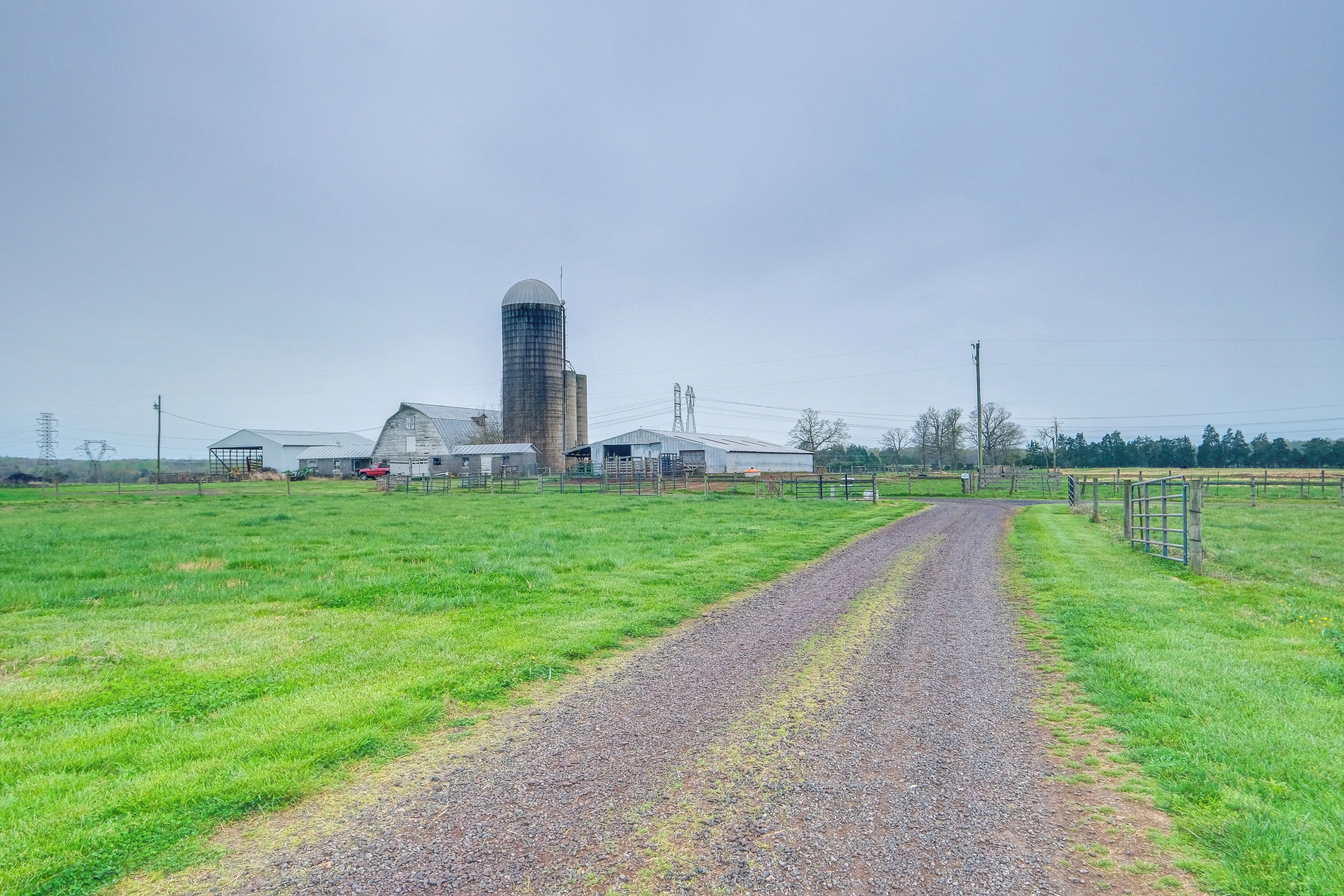 A rural road leading to a farm with barns and a silo.