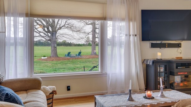 A living room with a large window, a television, a fireplace, and a table with candles. - Deck & Pasture Views! Bealeton Farmhouse Escape (Bealeton)