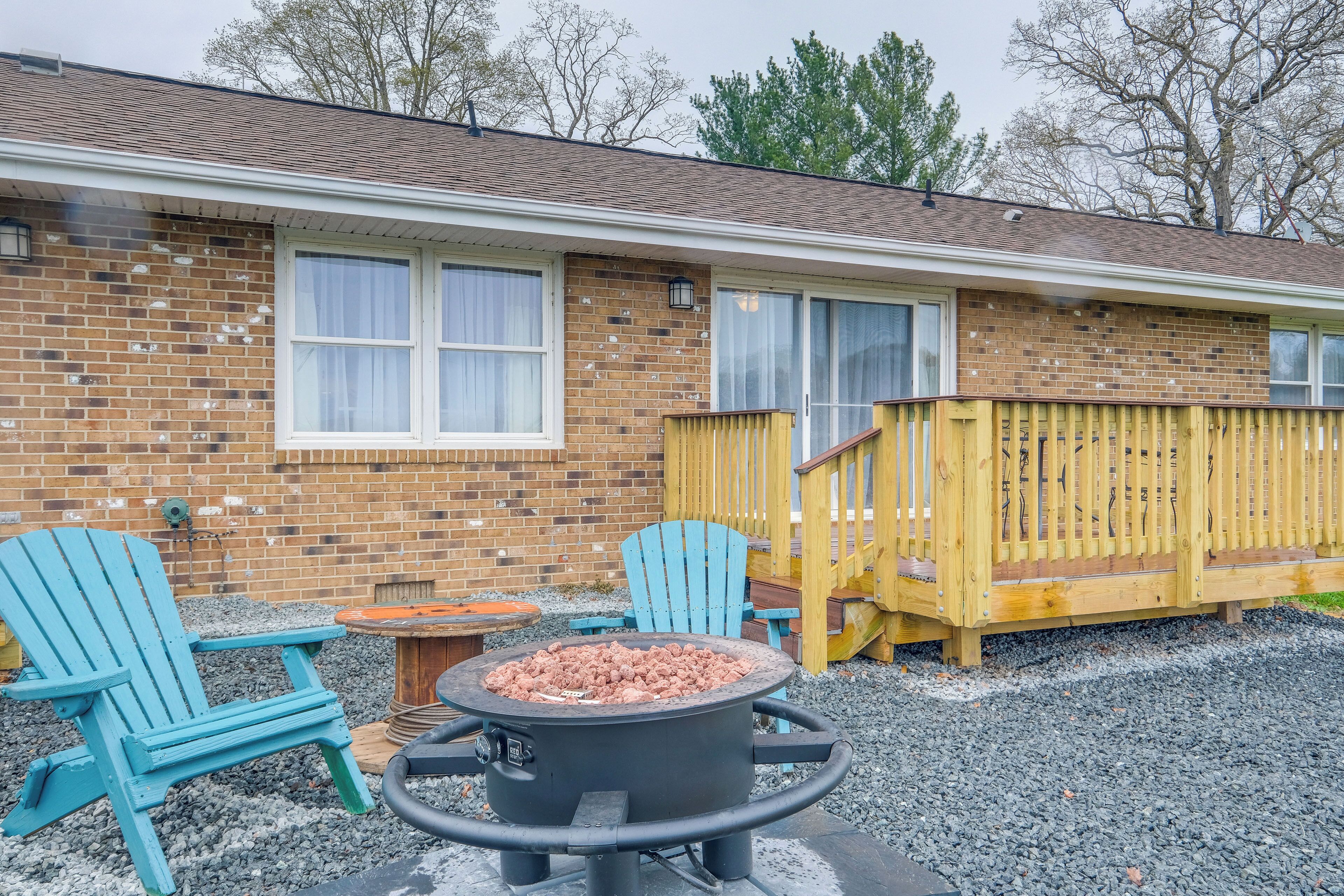 A brick house with a wooden deck, two Adirondack chairs, and a fire pit.