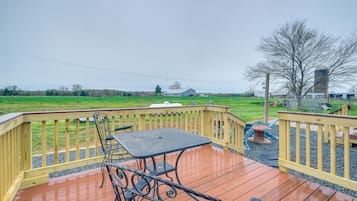 A wooden deck with a table and chairs, overlooking a green field and a distant building.