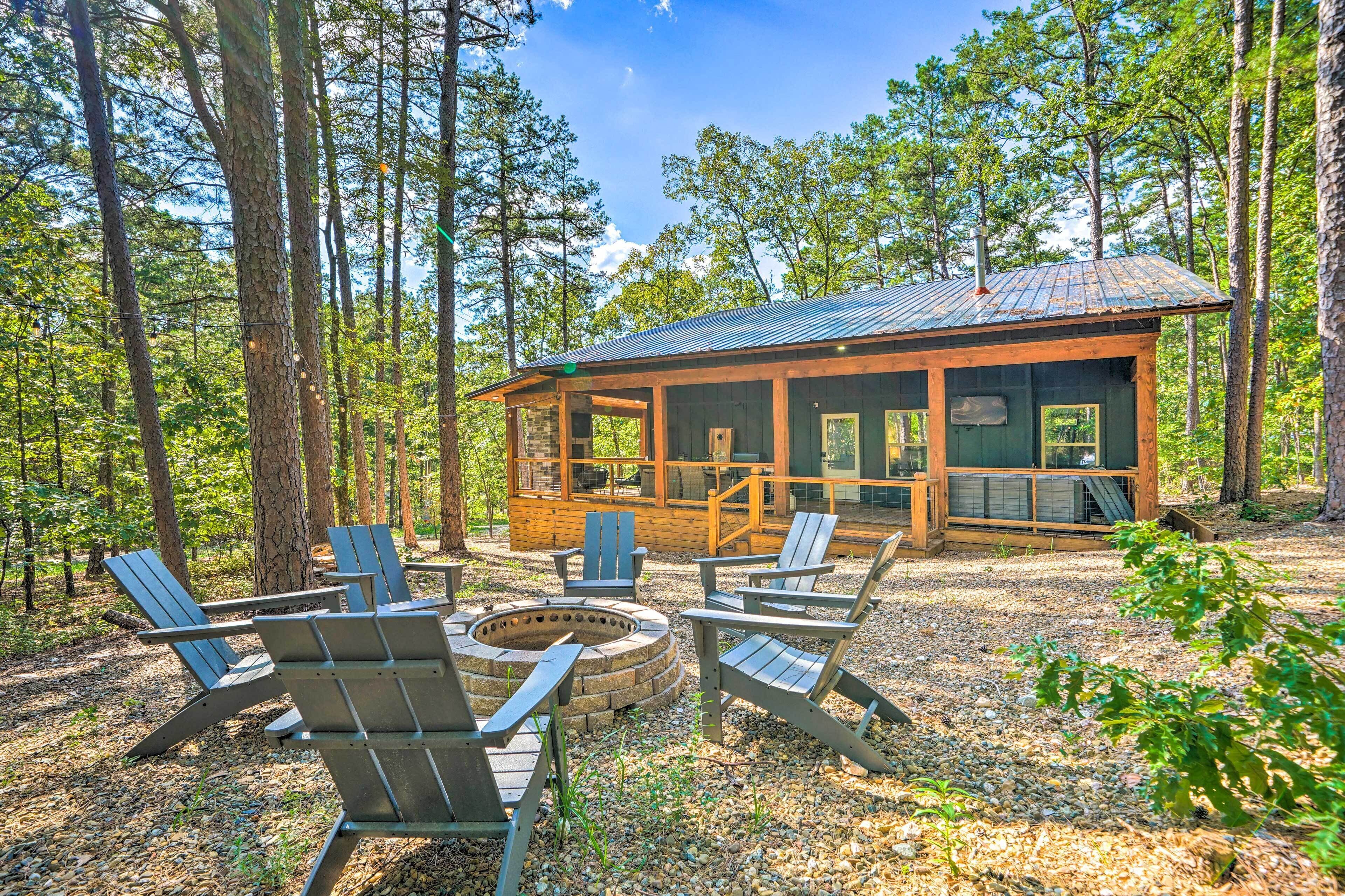 Une cabane avec un foyer et des fauteuils Adirondack, située dans un cadre forestier.