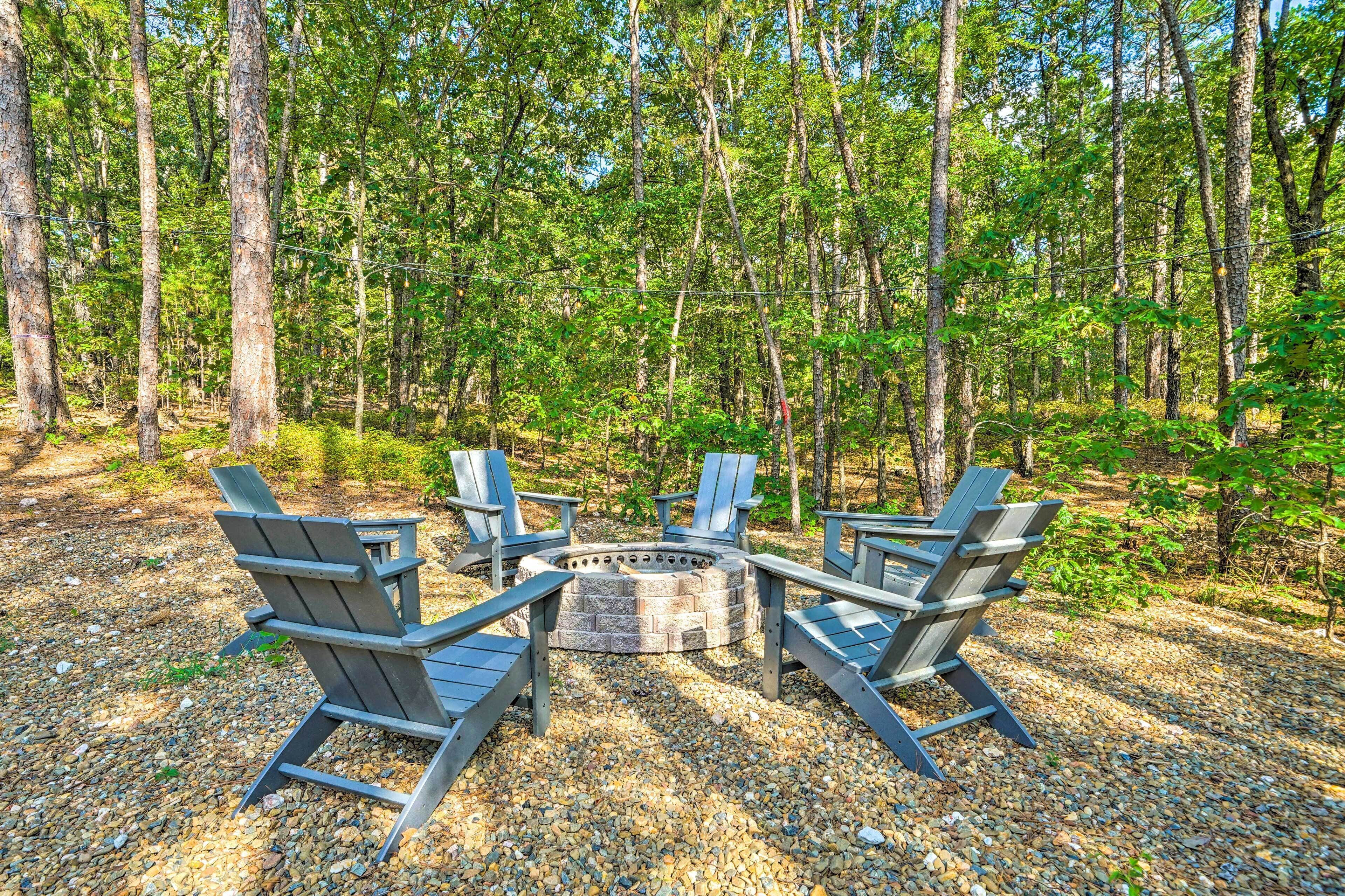 Un foyer circulaire, entouré de quatre chaises Adirondack, dans un cadre forestier.