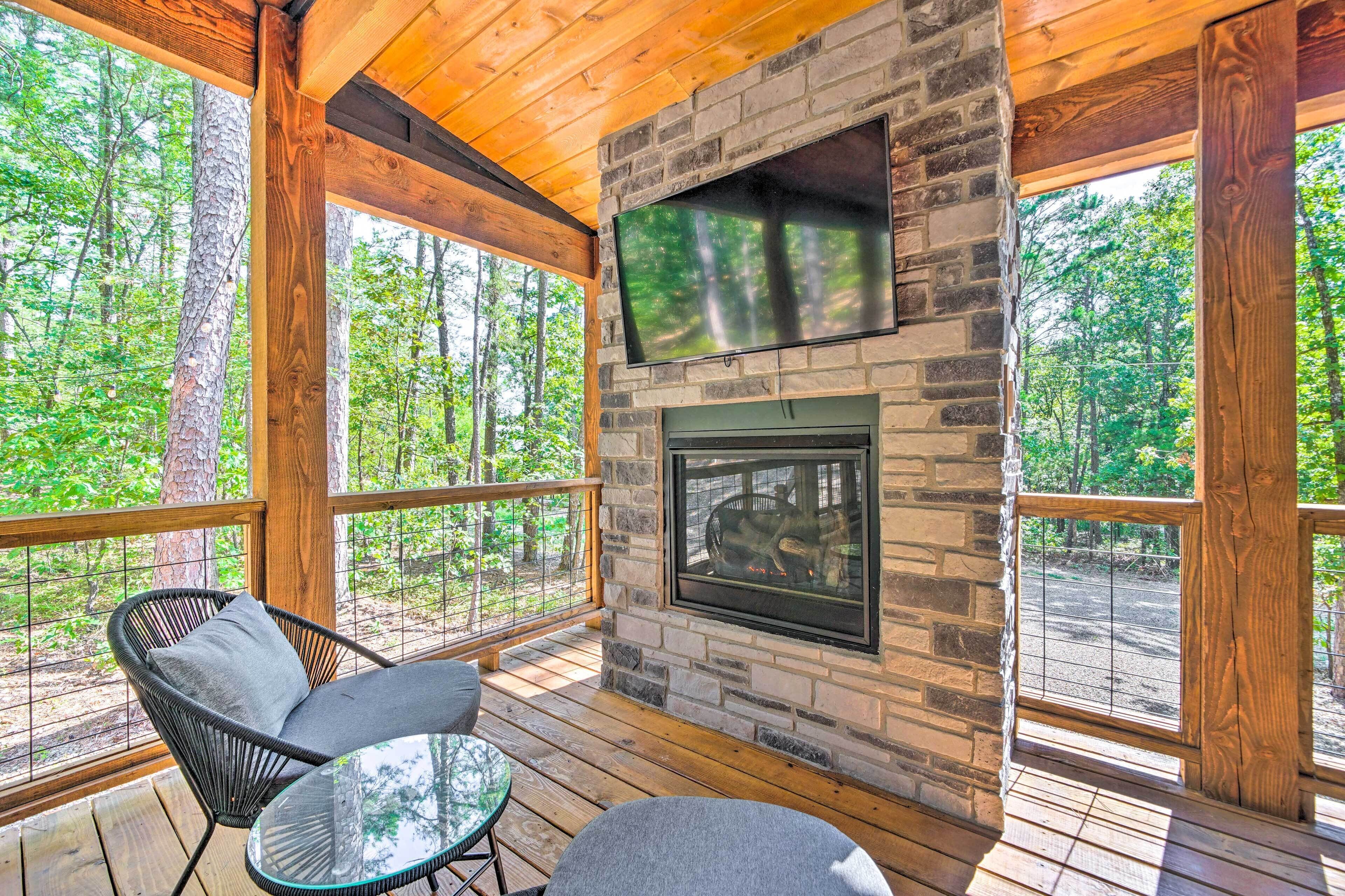 Una terraza de madera con chimenea de piedra, una televisión de pantalla plana y mobiliario exterior.