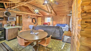 A cozy cabin interior with a wooden ceiling, a dining area with a round table and chairs, a sofa, and a kitchenette. - Cornell Home w/ Fire Pit & Hunting Access! (Cornell)