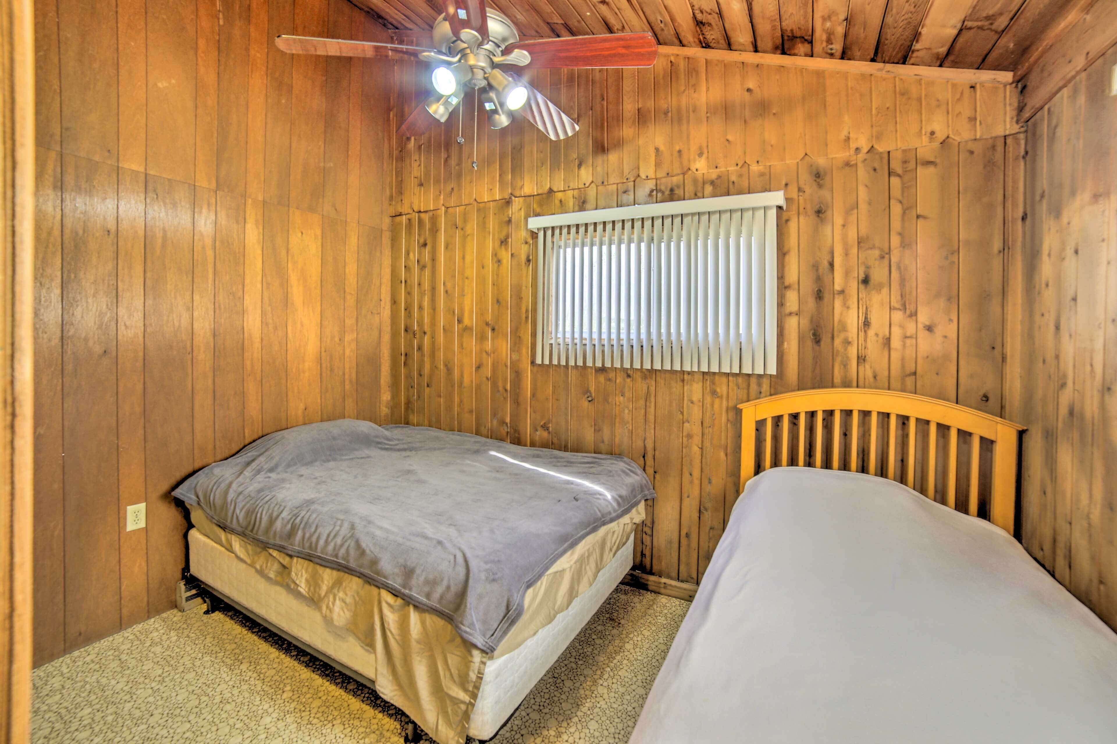 Una habitación de madera con una cama, un ventilador de techo y una ventana con persianas.