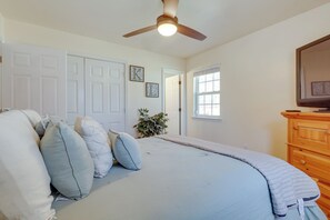 A bedroom with a bed, a ceiling fan, a window, and a wooden dresser.