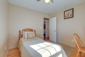 Een slaapkamer met een bed, een houten stoel, een deur en een lijst met een afbeelding aan de muur.