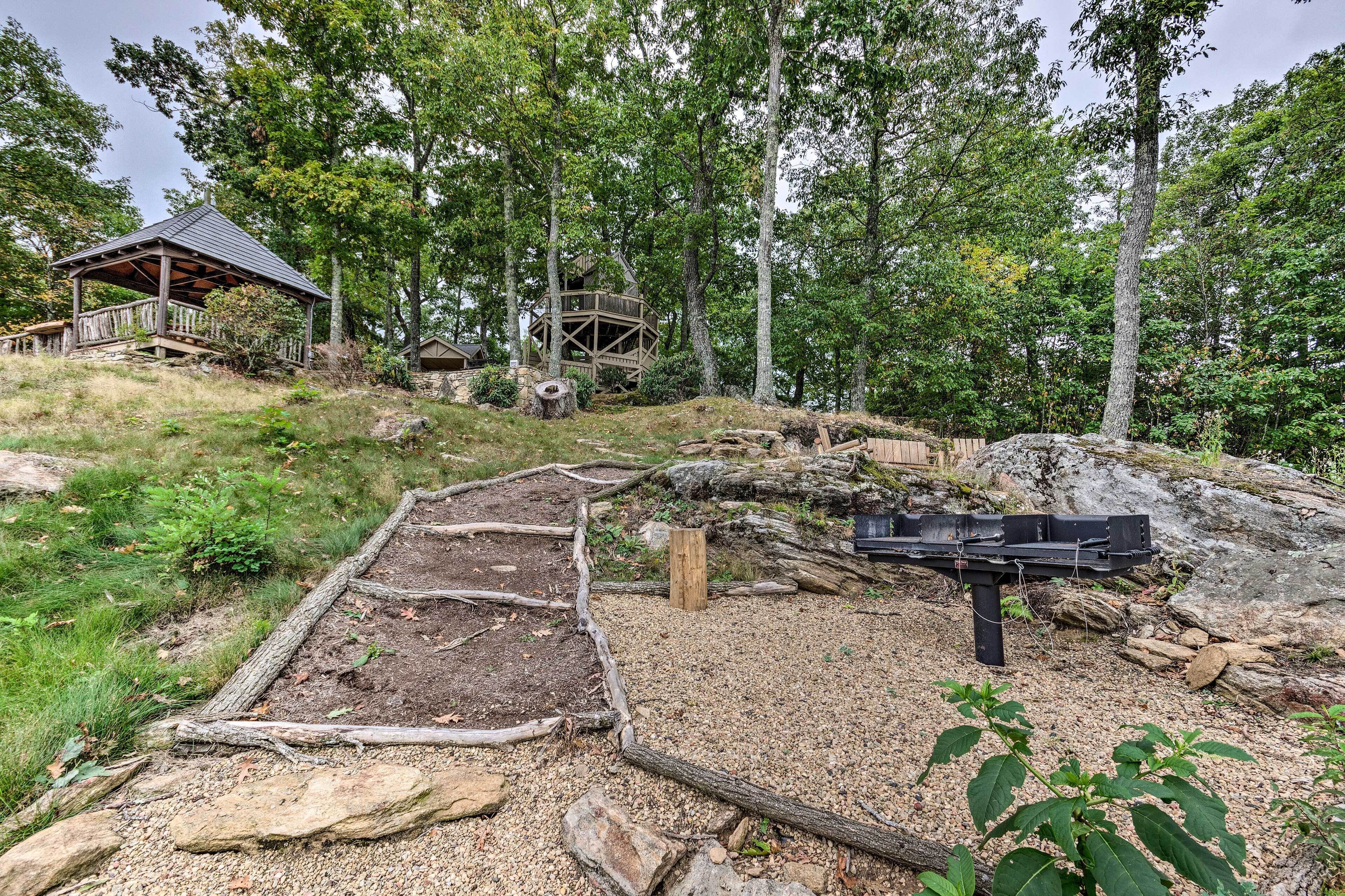 A rustic wooden structure with a covered porch, surrounded by a forested area with a dirt path leading to it.