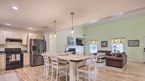 Een ruime keuken met moderne apparatuur, een eethoek met witte stoelen en een woonkamer met een bruine bank.