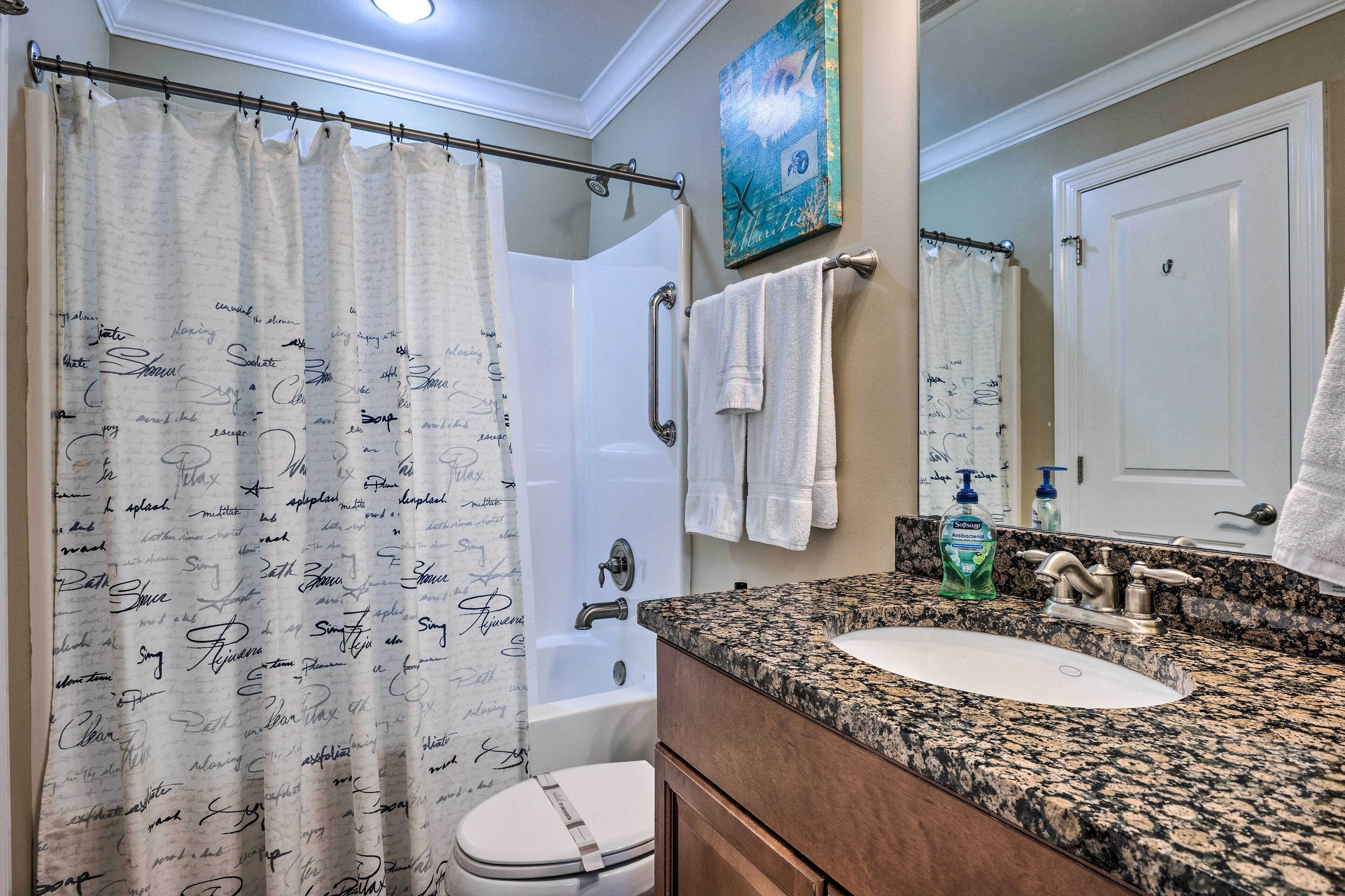 Une salle de bain avec un rideau de douche, une baignoire, des toilettes, un lavabo et un miroir.