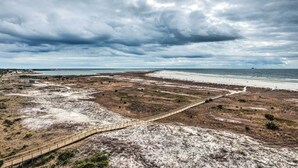 Un paisaje costero con una playa arenosa, un paseo marítimo de madera y un cielo nublado.