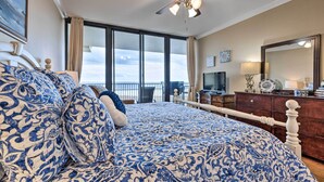 Un dormitorio con una cama grande, ventilador de techo, televisión y balcón con vistas.