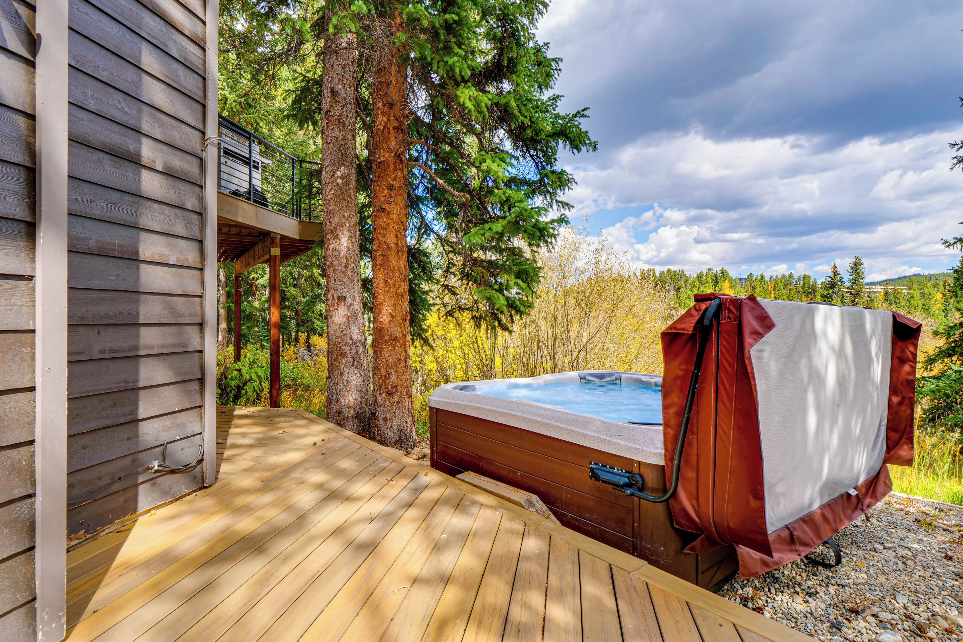 A wooden deck with a hot tub, surrounded by trees and a cloudy sky.