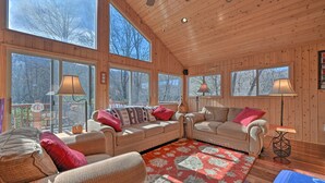 A cozy cabin interior with large windows, wooden walls, and a mix of seating areas.