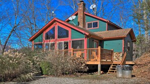A two-story cabin with a red and green exterior, a wooden deck, and satellite dishes on the roof.