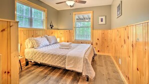 A bedroom with a bed, wooden walls, two windows with blinds, a ceiling fan, and a framed picture on the wall. - Hike & Zip-line: Red River Gorge Cabin w/ Hot Tub! (Zoe)
