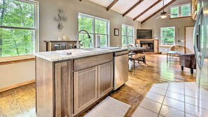 A spacious kitchen with a large island, wooden cabinets, and a stone countertop. There are multiple windows providing natural light and views of the outdoors. - Hike & Zip-line: Red River Gorge Cabin w/ Hot Tub! (Zoe)