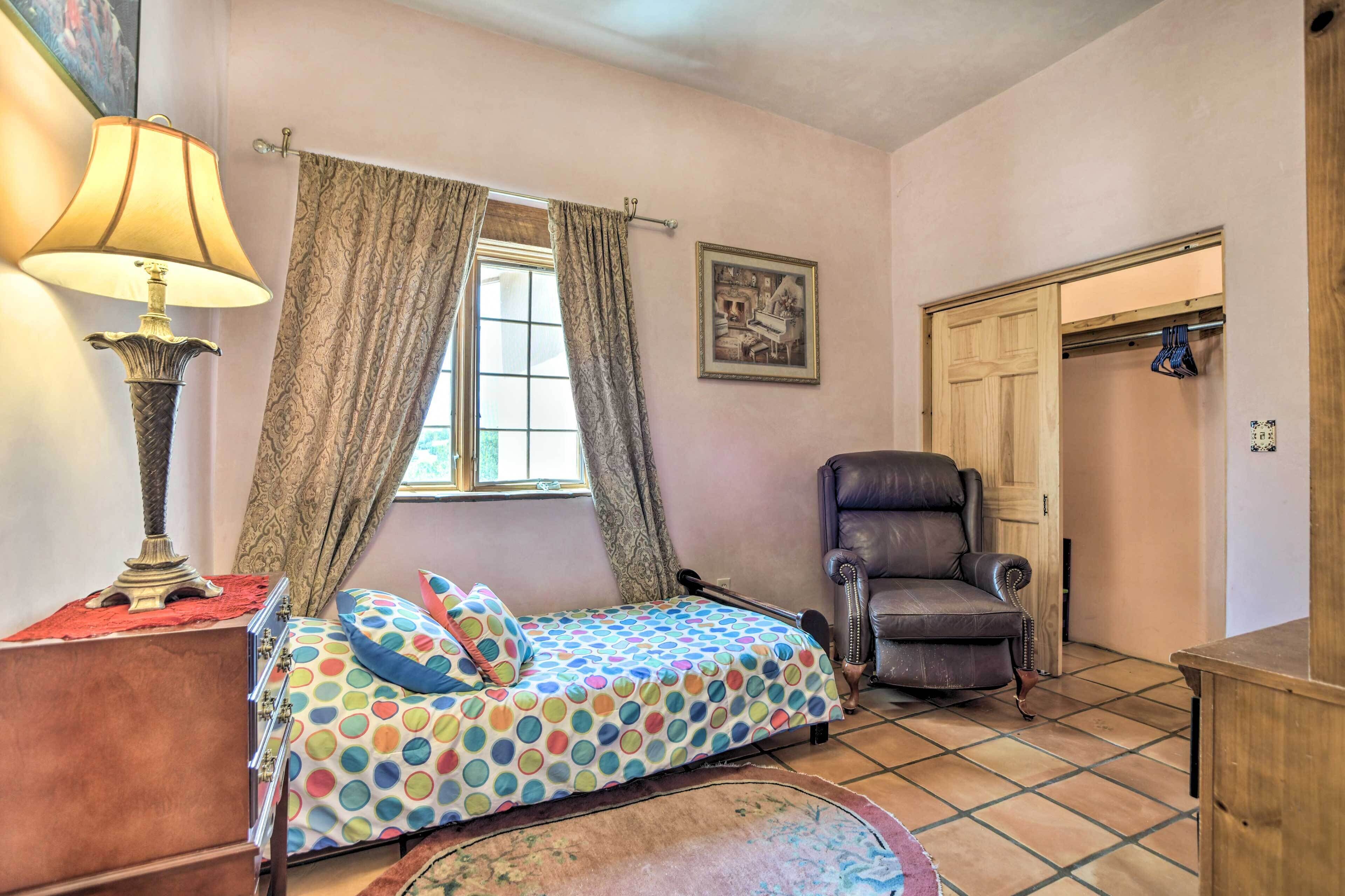 A bedroom with a bed, a chair, a lamp, a window with curtains, and a door.