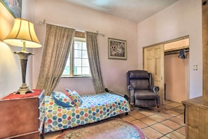 A bedroom with a bed, a chair, a lamp, a window with curtains, and a door.