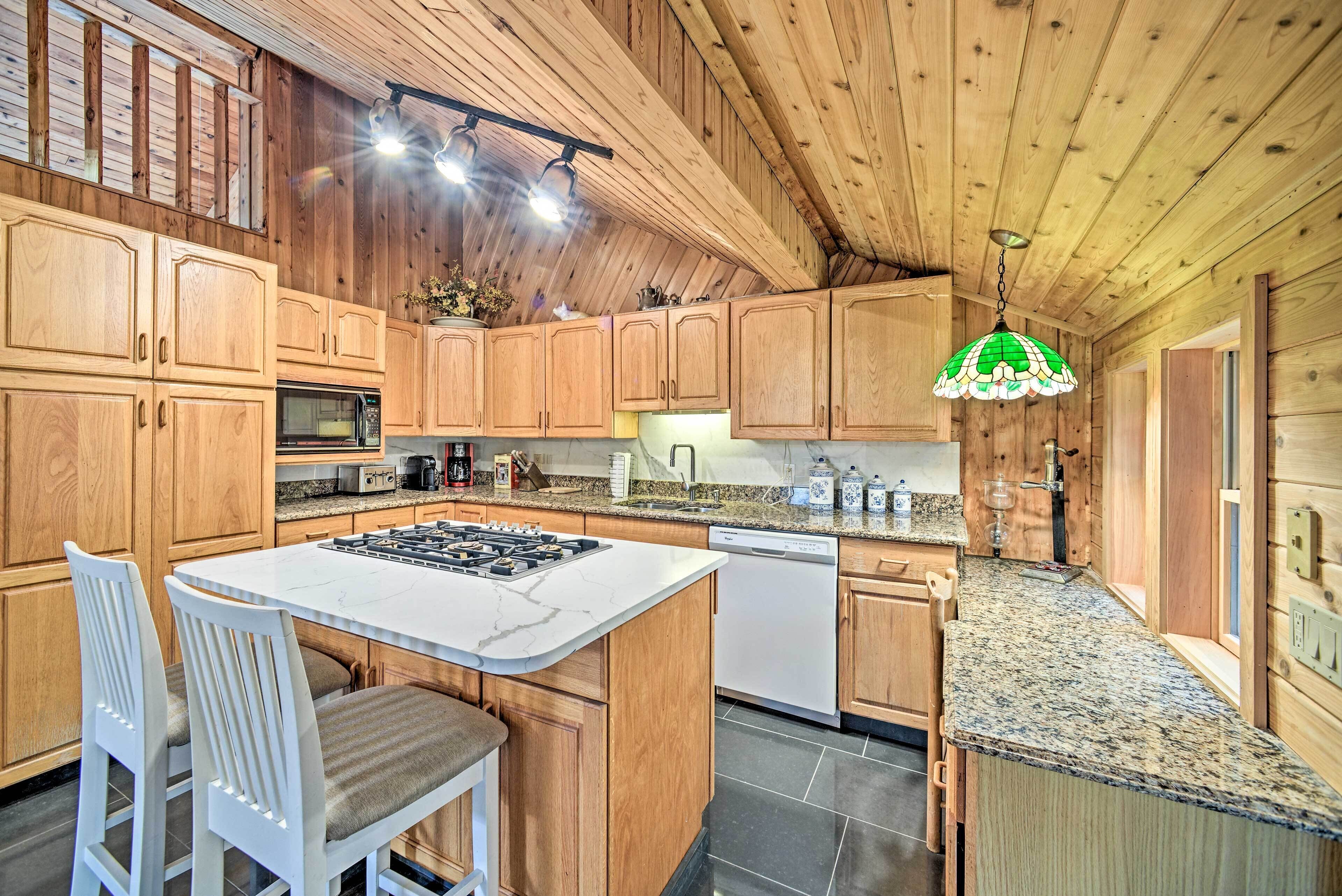 A kitchen with wooden cabinets, a granite countertop, a central island with a stove, and a hanging green light fixture.