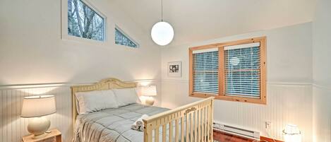 Un dormitorio con una cama de madera, dos mesitas de noche con lámparas, una ventana con persianas y un radiador.