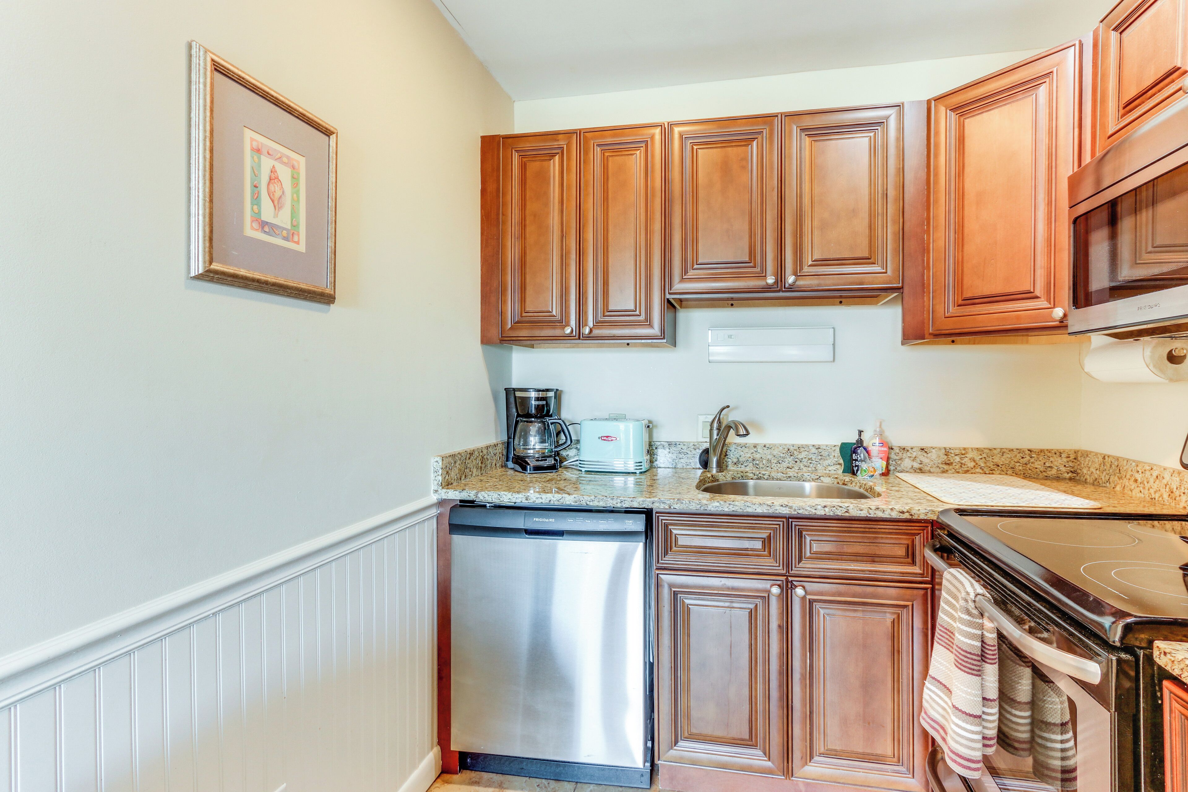 A compact kitchen with wooden cabinets, a dishwasher, a coffee maker, and a microwave.