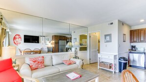 A modern living room with a sofa, a red chair, a coffee table, and a kitchen area with cabinets and appliances. - Ocean-view Balcony: Beachfront Hilton Head Condo (Hilton Head Island)