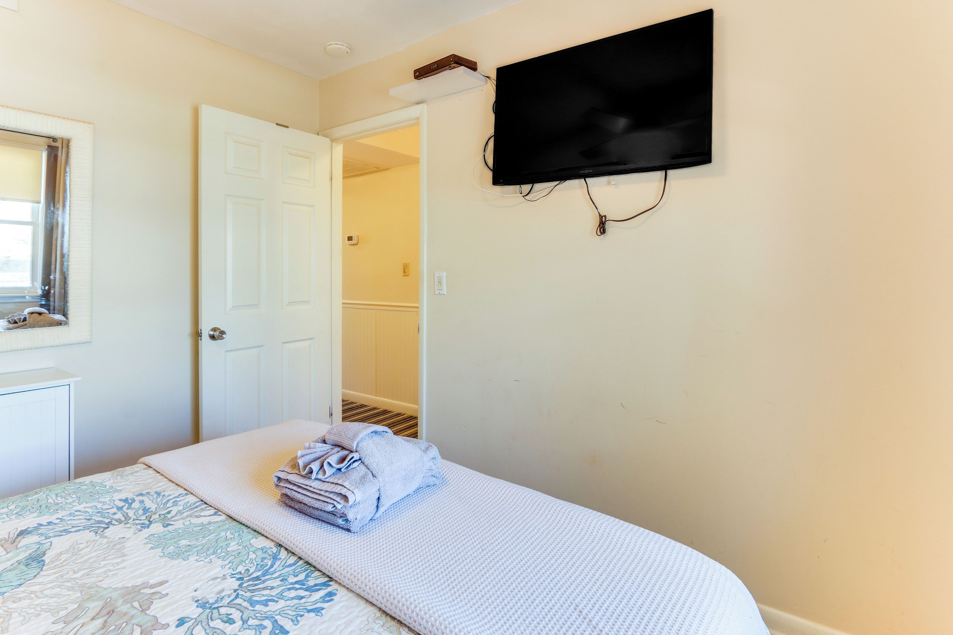 A bedroom with a bed, a TV mounted on the wall, and a door leading to another room.
