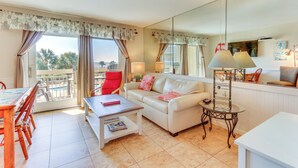 A living room with a white sofa, red chair, and a glass table. There is a balcony with a view of palm trees. - Ocean-view Balcony: Beachfront Hilton Head Condo (Hilton Head Island)