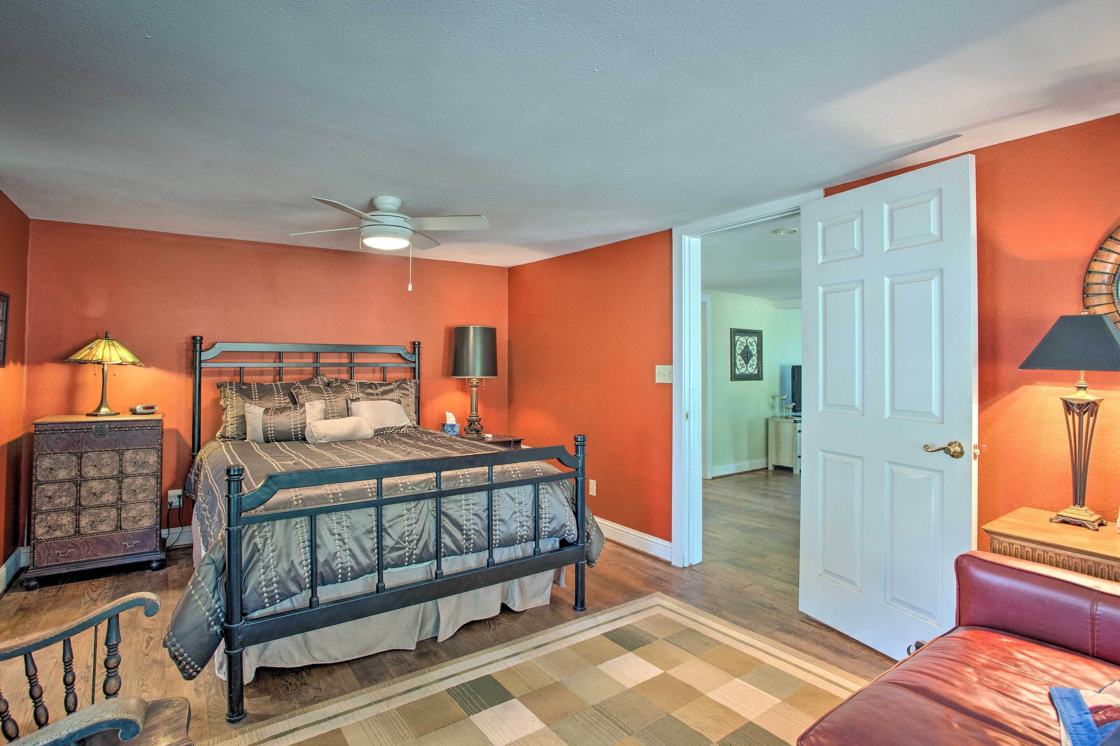 A bedroom with a bed, a dresser, a lamp, and a door leading to another room.