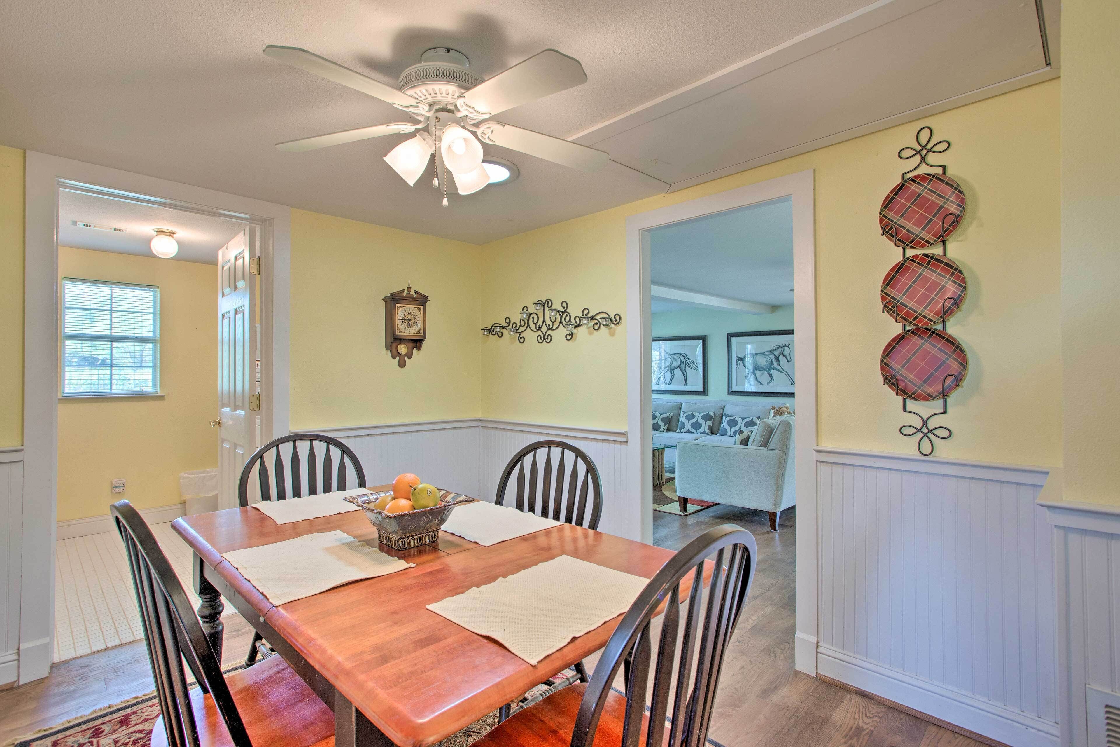 A dining room with a wooden table, four chairs, a ceiling fan, and a wall clock.