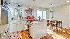 Una cocina con armarios blancos, una isla central y una zona de comedor con una mesa y sillas de madera.