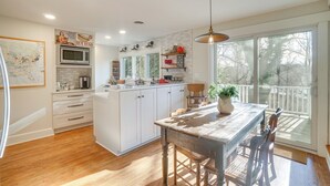 Una cocina moderna con armarios blancos, una isla central y un amplio ventanal con vista a una terraza.