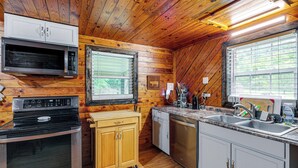 A kitchen with wooden walls, a microwave, oven, wooden cabinets, a dishwasher, and a window with blinds. - Peaceful + Cozy Cottage on Over 7 Acres w/ Creek (Lenoir)