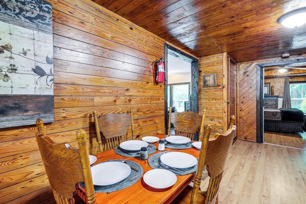 Une salle à manger aux murs lambrés, avec une table dressée pour quatre personnes, des chaises et un extincteur fixé au mur.