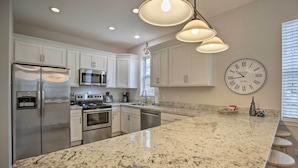 A modern kitchen with white cabinets, stainless steel appliances, a granite countertop, and a wall clock.