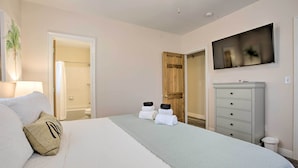 A bedroom with a bed, a dresser, a TV, and a door leading to a bathroom.