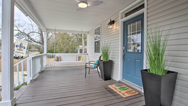 A covered porch with a ceiling fan, a blue door, and two large planters.